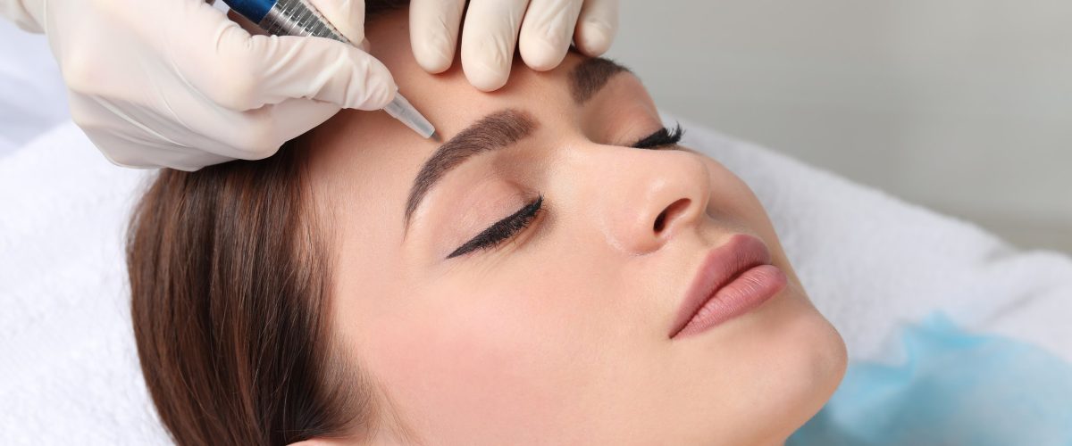 Young woman during procedure of permanent eyebrow makeup in beauty salon, closeup